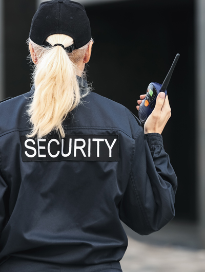 female security guard in uniform holding radio communication device while monitoring surroundings