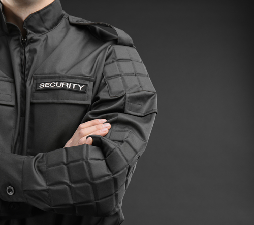 person wearing a security uniform with arms crossed showing a black textured fabric and security label