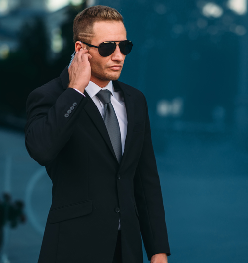 man in black suit with sunglasses holding earpiece standing confidently in urban setting security detail professional