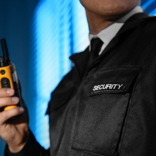 man in security uniform holding a walkie talkie standing near windows showcasing professional security personnel