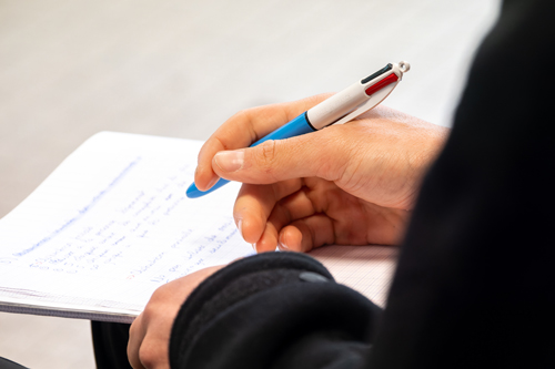 hand holding a blue pen over notebook with notes