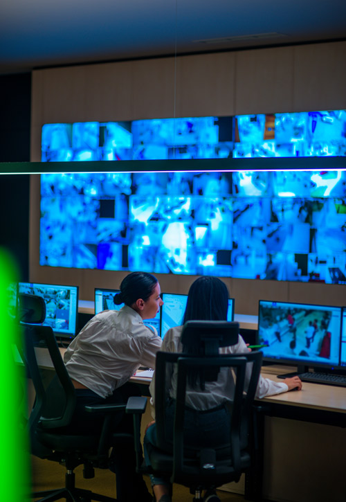 two professionals analyzing surveillance data on multiple monitors in a modern control room setting