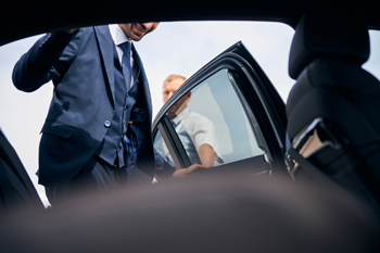 man in a suit opening car door with another person inside luxury car transport service